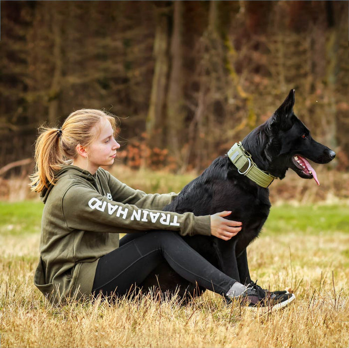 Hundeführerin mit Schäferhund im olivem Trainings-Hoodie beim Outdoor-Training
